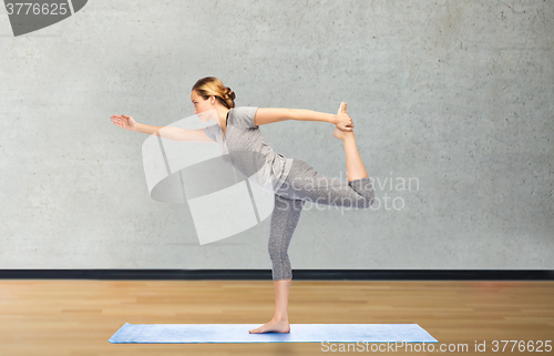 Image of woman making yoga in lord of the dance pose on mat