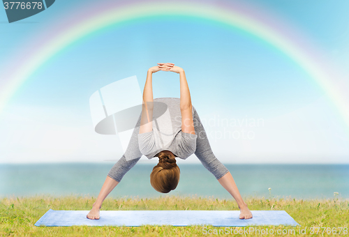 Image of woman making yoga wide-legged forward bend on mat