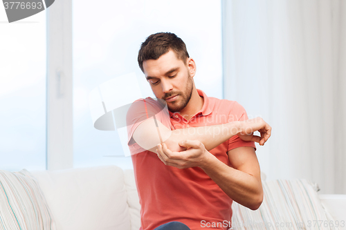 Image of unhappy man suffering from pain in hand at home