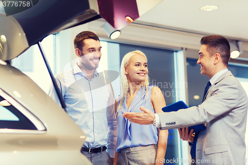 Image of happy couple with car dealer in auto show or salon