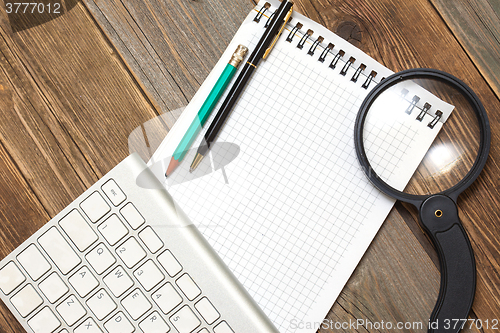 Image of notebook, computer keyboard, magnifying glass and a pencil with 