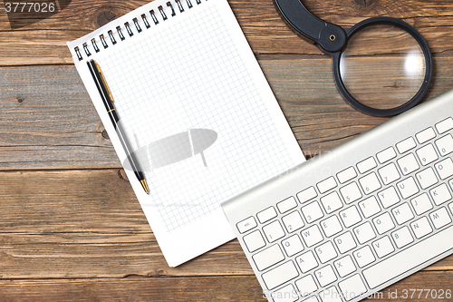 Image of still life with note pad, computer keyboard, magnifying glass an