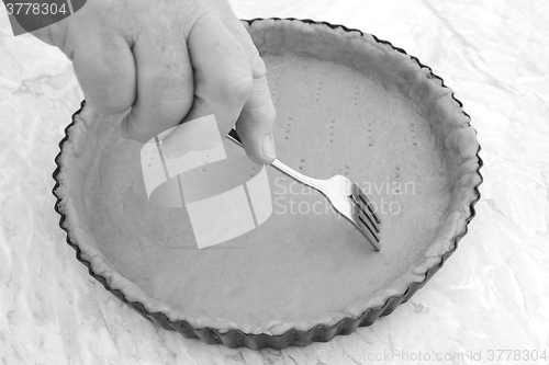 Image of Woman using fork to prick holes in an uncooked pie crust