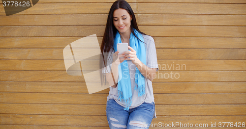 Image of Woman texting while leaning against wall