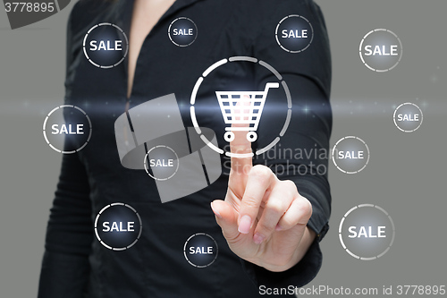 Image of Beautiful Woman Pointing at Glowing Shopping Cart Icon. Business Concept. button sale