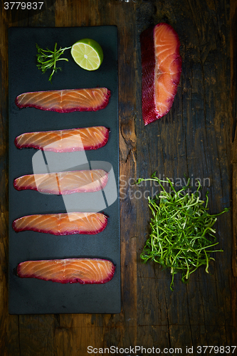 Image of Sliced salmon fillet, sauteed with beetroot juice over black slate surface.
