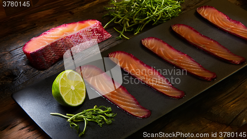 Image of Sliced salmon fillet, sauteed with beetroot juice over black slate surface.