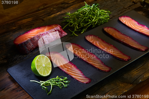Image of Sliced salmon fillet, sauteed with beetroot juice over black slate surface.