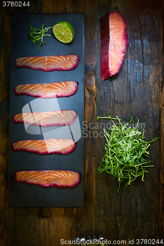 Image of Sliced salmon fillet, sauteed with beetroot juice over black slate surface.