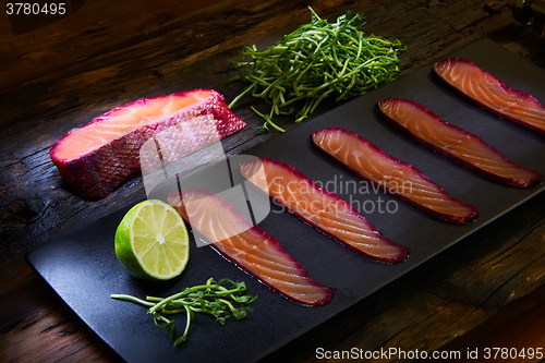 Image of Sliced salmon fillet, sauteed with beetroot juice over black slate surface.