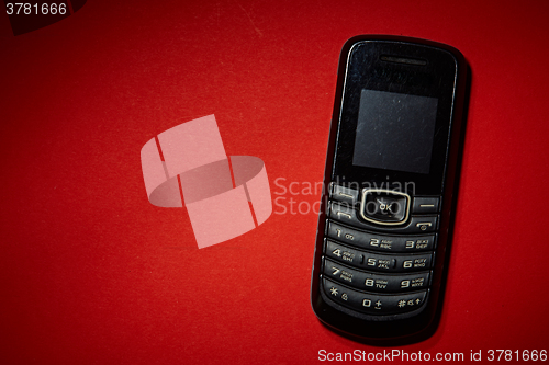 Image of Old black cell phone on the red background.
