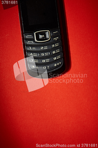 Image of Old black cell phone on the red background.