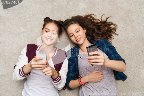 Image of happy teenage girls lying on floor with smartphone