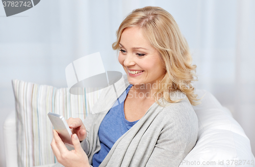 Image of smiling woman with smartphone texting at home