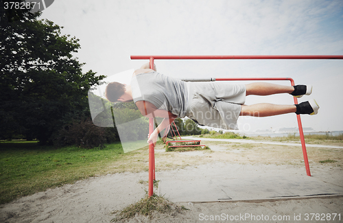 Image of young man exercising on parallel bars outdoors