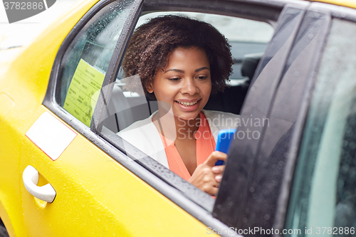 Image of happy african woman texing on smartphone in taxi