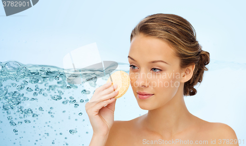 Image of young woman cleaning face with exfoliating sponge