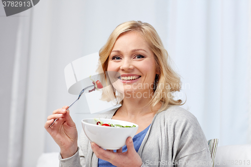 Image of smiling middle aged woman eating salad at home