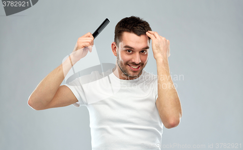 Image of happy man brushing hair with comb over gray