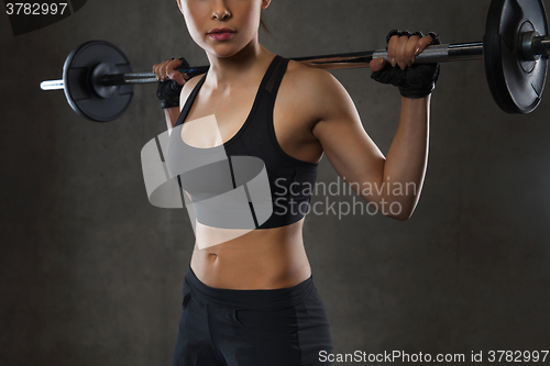 Image of young woman flexing muscles with barbell in gym