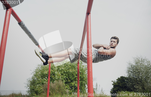 Image of young man doing sit up on parallel bars outdoors