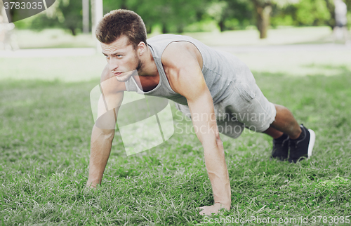 Image of young man doing push ups on grass in summer park