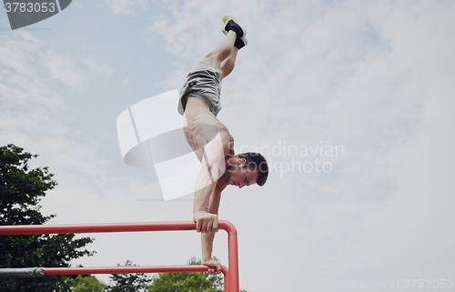 Image of young man exercising on parallel bars outdoors