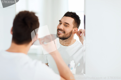 Image of man cleaning ear with cotton swab at bathroom