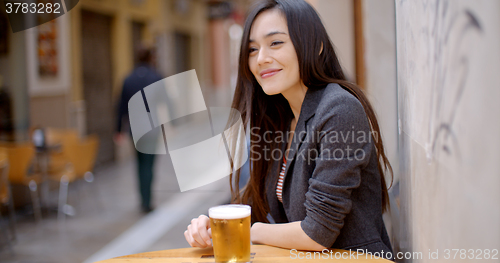 Image of Friendly young woman sitting enjoying a beer