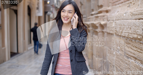 Image of Young woman walking through town with her mobile