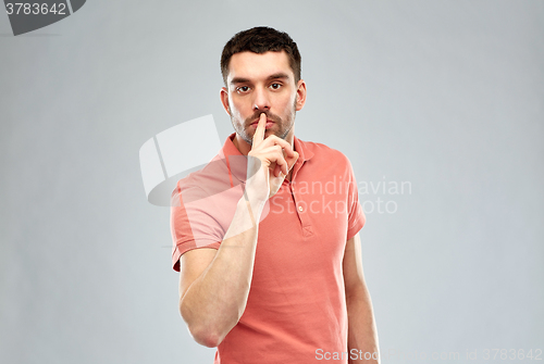 Image of young man making hush sign over gray background