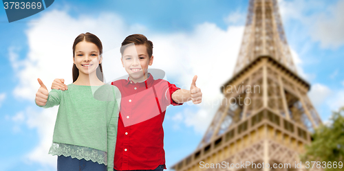 Image of boy and girl showing thumbs up over eiffel tower