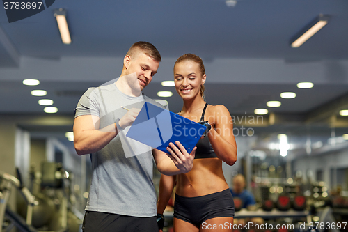 Image of smiling young woman with personal trainer in gym