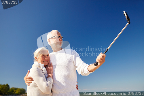 Image of seniors with smartphone taking selfie on beach