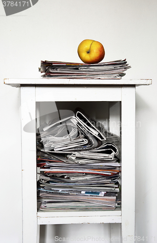 Image of stack of newspapers on the nightstand and an apple