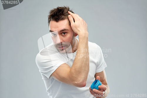 Image of happy young man styling his hair with wax or gel