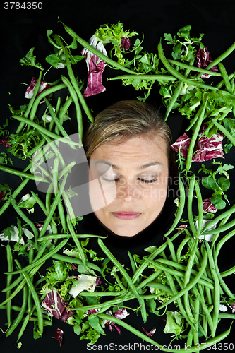 Image of Cute blond girl shot in studio with vegetables aroound the head