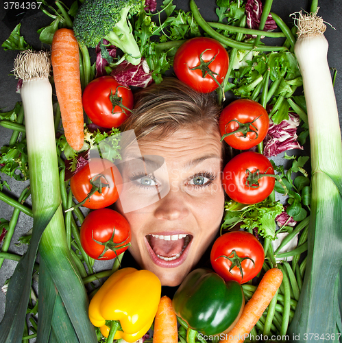 Image of Cute blond girl shot in studio with vegetables aroound the head