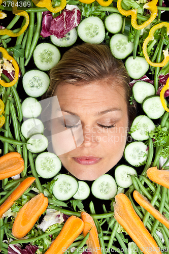 Image of Cute blond girl shot in studio with vegetables aroound the head