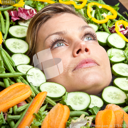 Image of Cute blond girl shot in studio with vegetables aroound the head