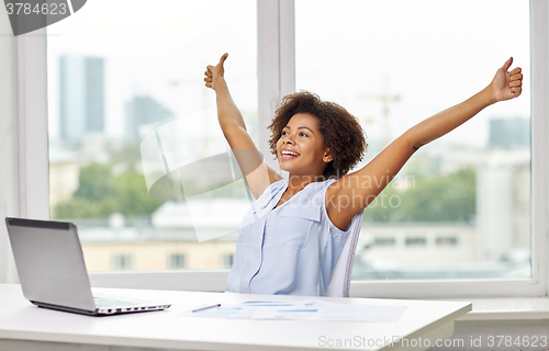 Image of happy african woman with laptop at office