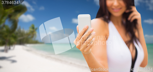 Image of young woman taking selfie with smartphone on beach