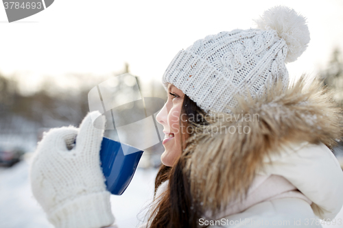 Image of happy young woman with tea cup outdoors in winter