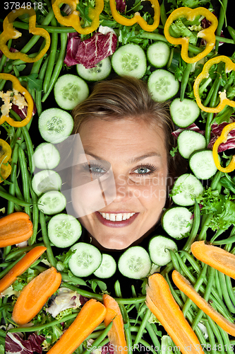 Image of Cute blond girl shot in studio with vegetables aroound the head