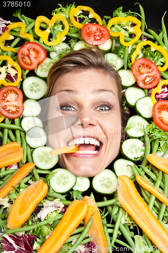 Image of Cute blond girl shot in studio with vegetables aroound the head