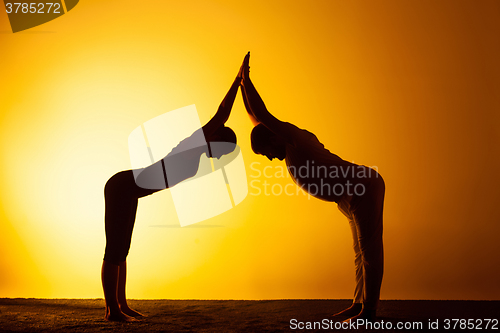 Image of Two people practicing yoga in the sunset light