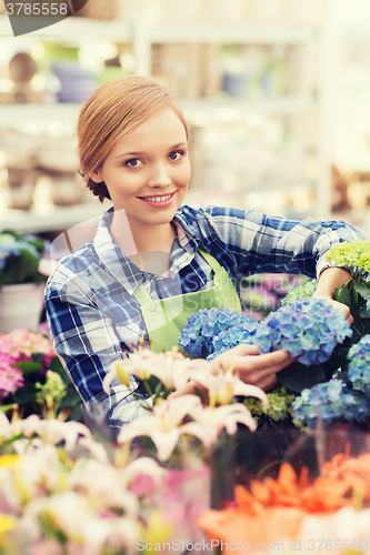 Image of happy woman taking care of flowers in greenhouse