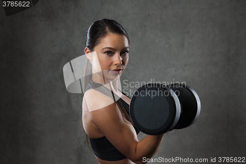 Image of young woman flexing muscles with dumbbells in gym