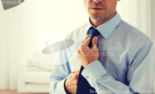 Image of close up of man in shirt adjusting tie on neck