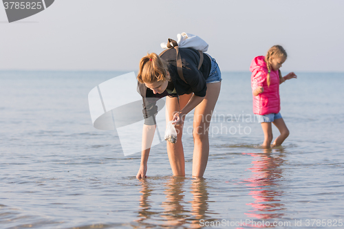 Image of Woman with child walking along the beach and collect seashells